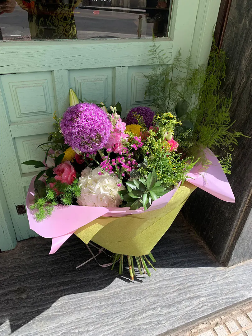 Déjate sorprender por la magia del ramo Teodora, una composición llena de colores vibrantes y texturas que evocan lo mejor de la primavera. Este ramo espectacular combina la fuerza esférica del Allium, la elegancia de las Peonías, la delicadeza de las Anastasias y el encanto romántico de las Hortensias. Los Alhelíes y Liliums aportan aroma y verticalidad, mientras que los verdes decorativos cuidadosamente seleccionados enmarcan cada flor, creando una pieza armónica y llena de vida.